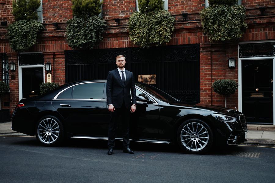 Chauffeur wearing a dark suit beside a Mercedes-Benz S-Class