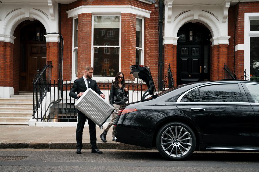 Chauffeur lifting a silver suitcase beside a Mercedes-Benz S-Class outside a London house