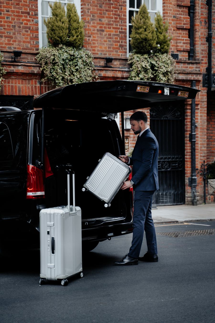 Chauffeur loading a silver suitcase into a Mercedes-Benz V-Class with the boot open