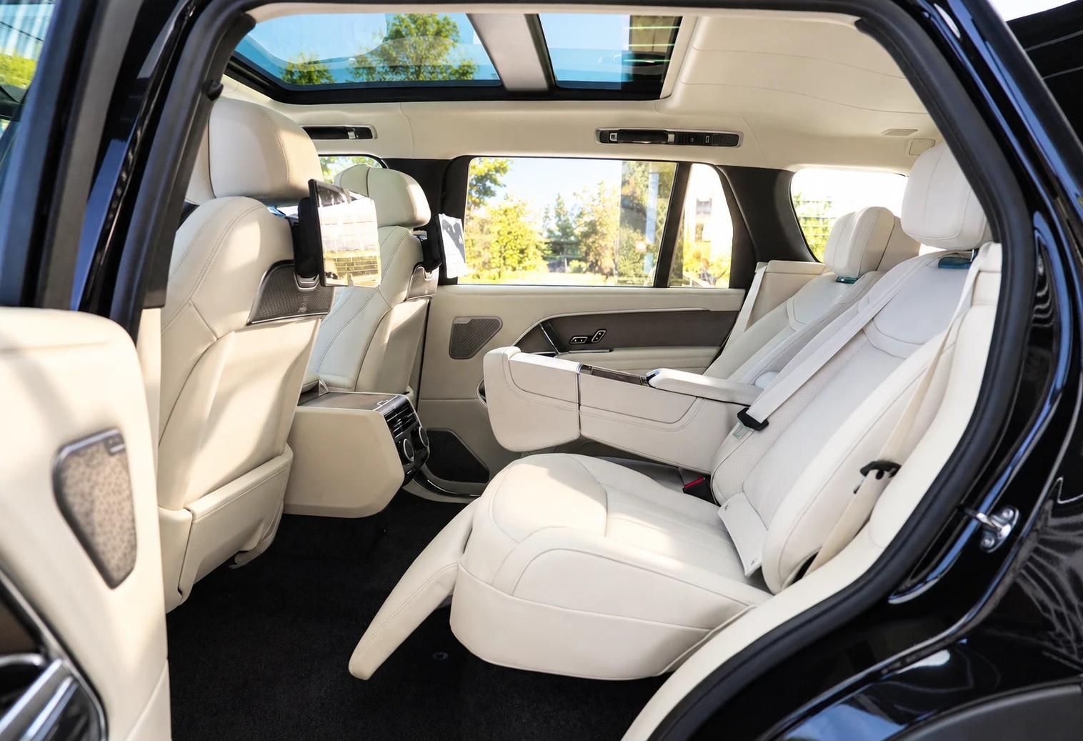 Rear cabin of a black Range Rover with cream leather seats and two rear screens